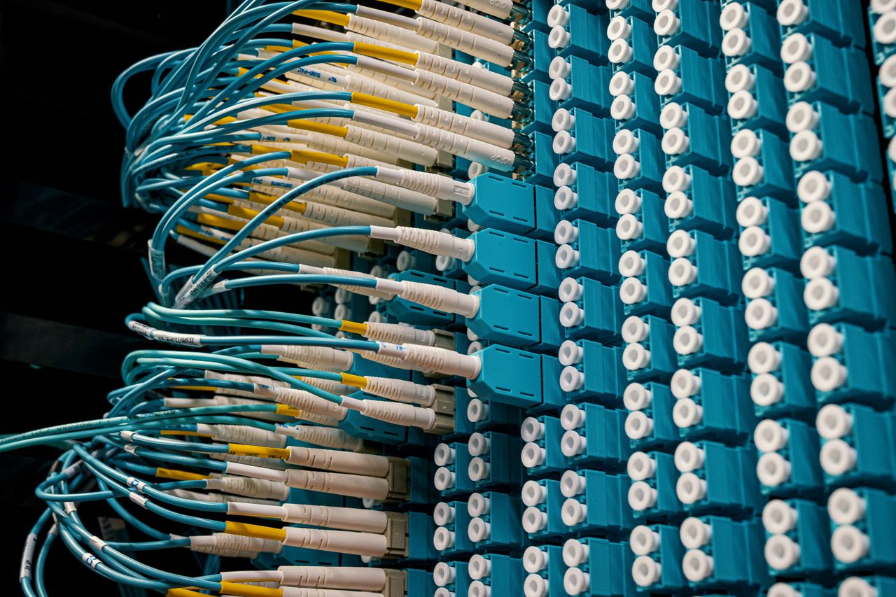 about-us Detailed view of fiber optic patch cables connecting to a blue patch panel in a data center.